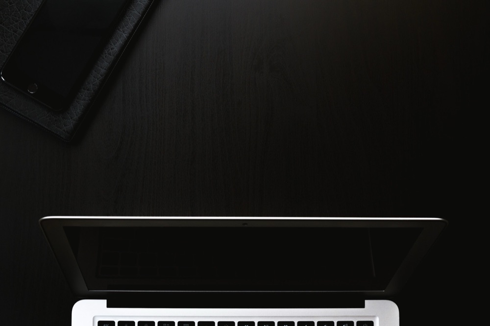 A laptop and smartphone on a dark, minimal desk