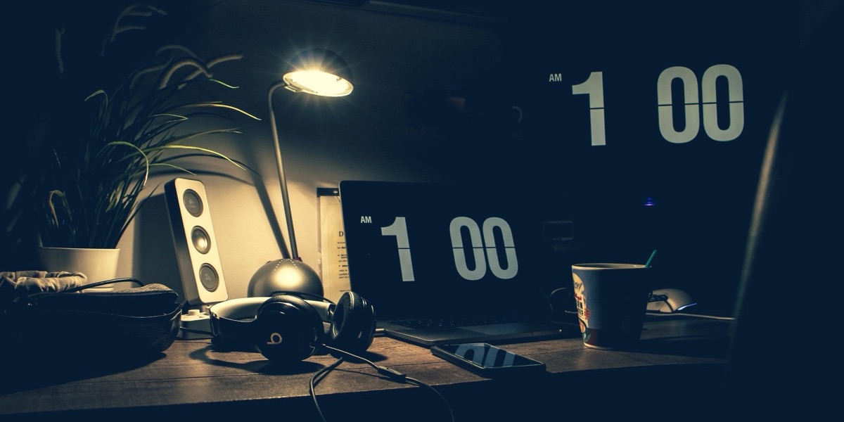 A dimly lit desk with a laptop and headphones late at night