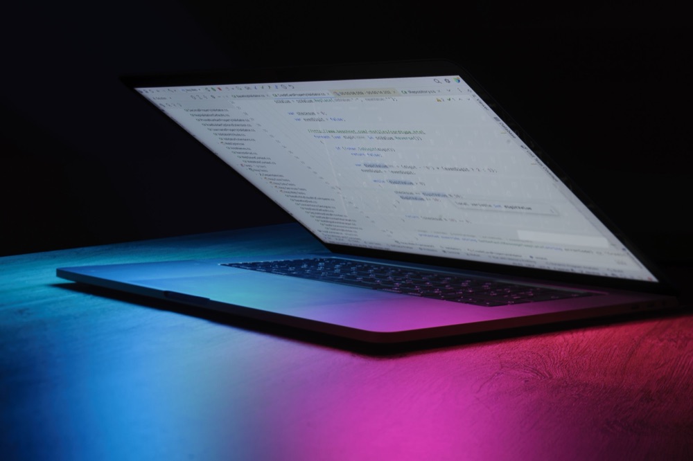 A laptop displaying code lit by neon light in a dark room