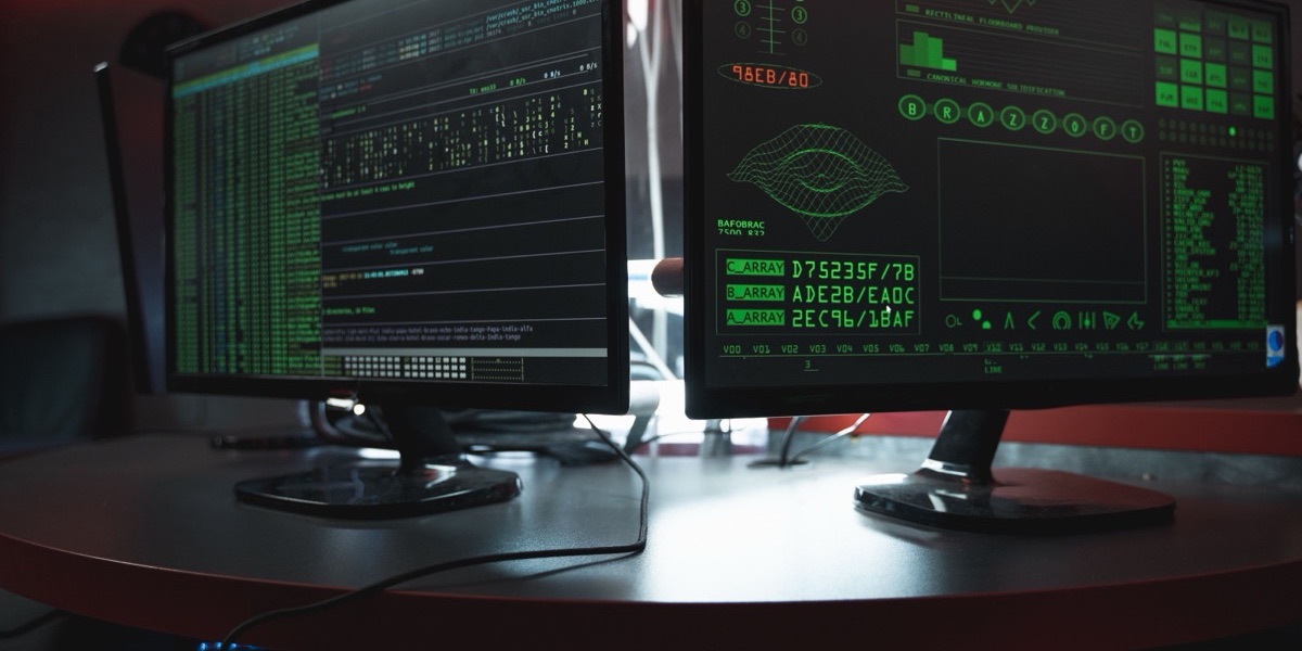 Two computer monitors filled with code in a dark room